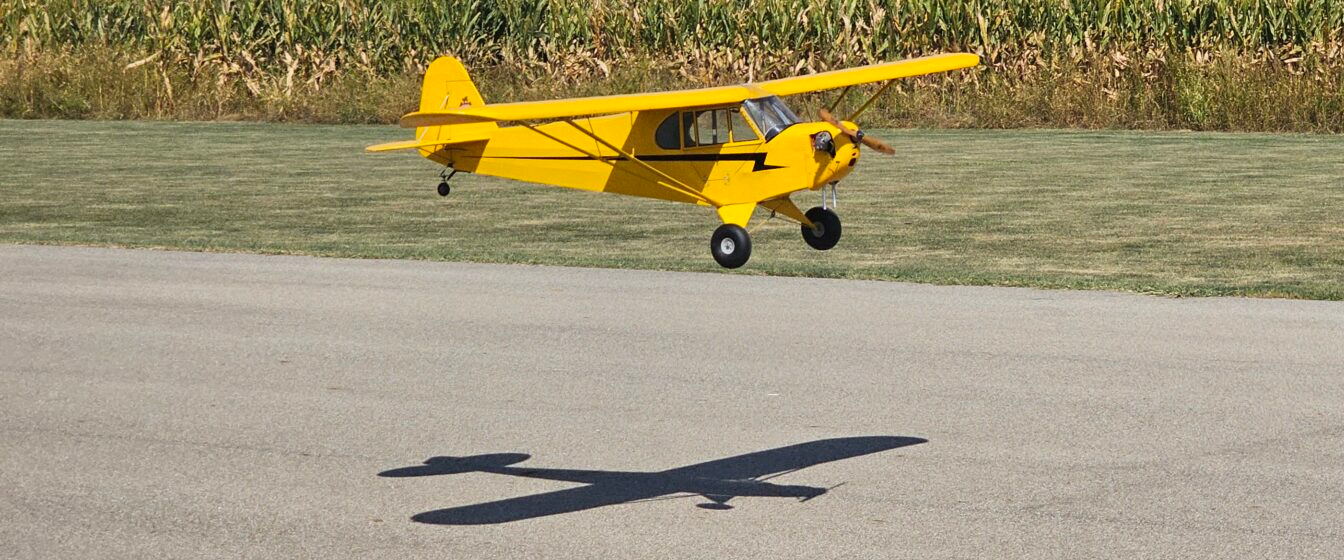 Yellow RC airplane approaching the runway with its shadow visible below