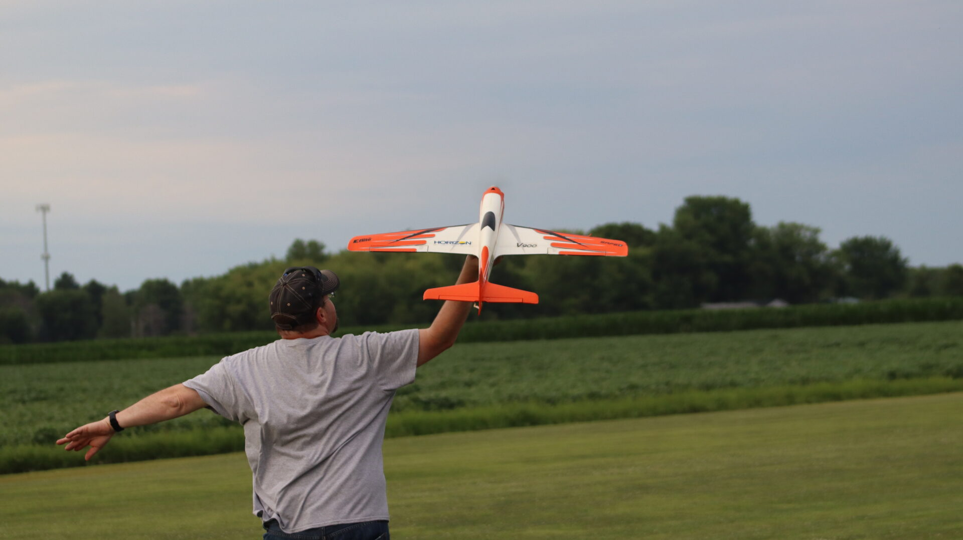 Modeler hand launching a red-and-white RC airplane over a grass flying field