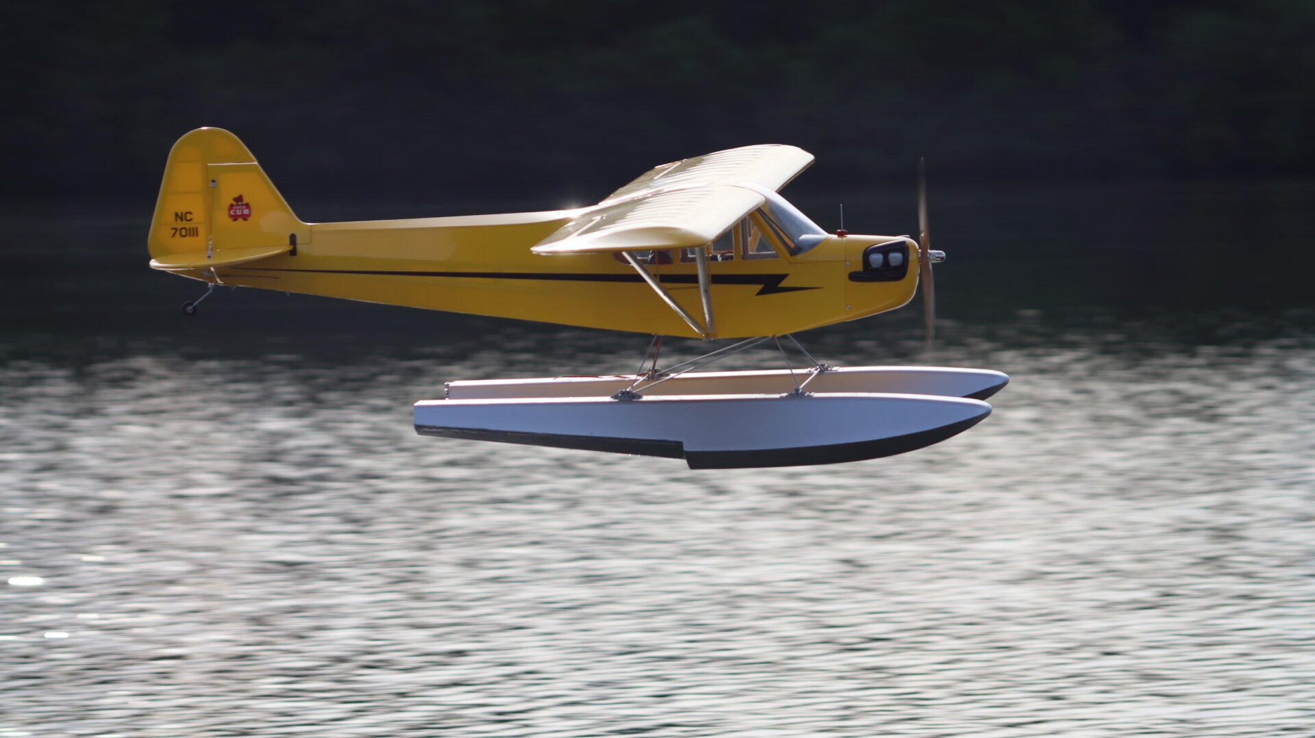 Yellow Hangar 9 J-3 Cub flying low above the lake on silver floats